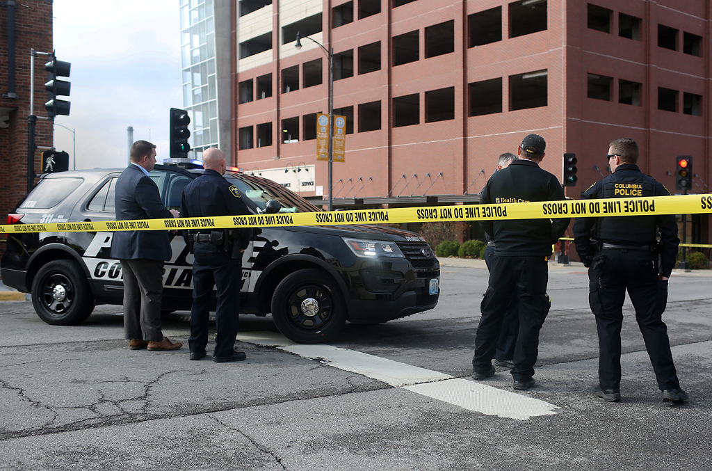 Columbia Police officers and a staff member of MU Health Care EMS gather behind police tape